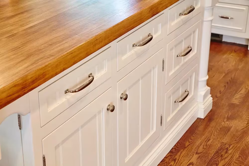 Cream cabinet drawers with brass cup pulls under a butcher block counter
