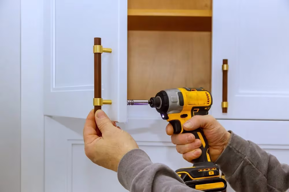 Hands fitting a brass bar pull to a white door with a drill