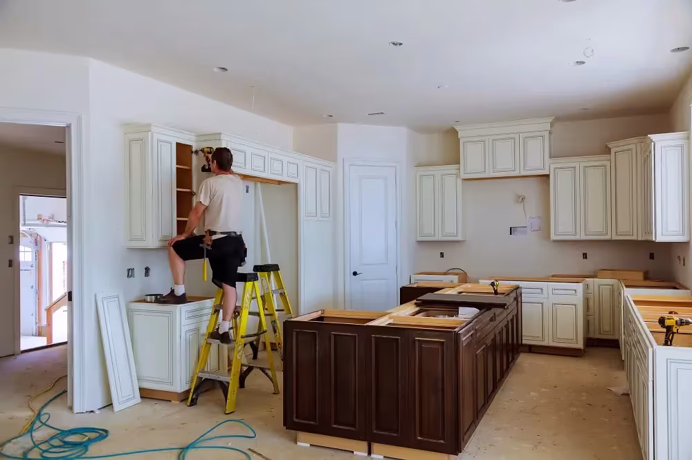 Cream kitchen mid-refacing with a worker on a step ladder