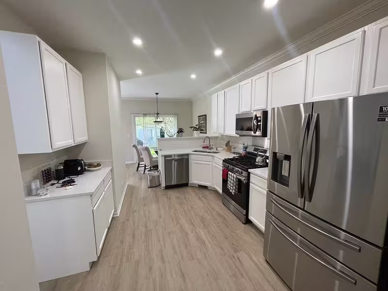 White refaced cabinets and a stainless refrigerator in the finished kitchen