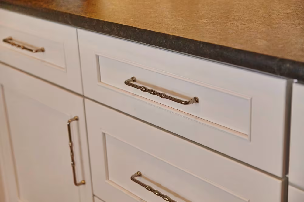 White drawer fronts with brass bar pulls under a dark counter