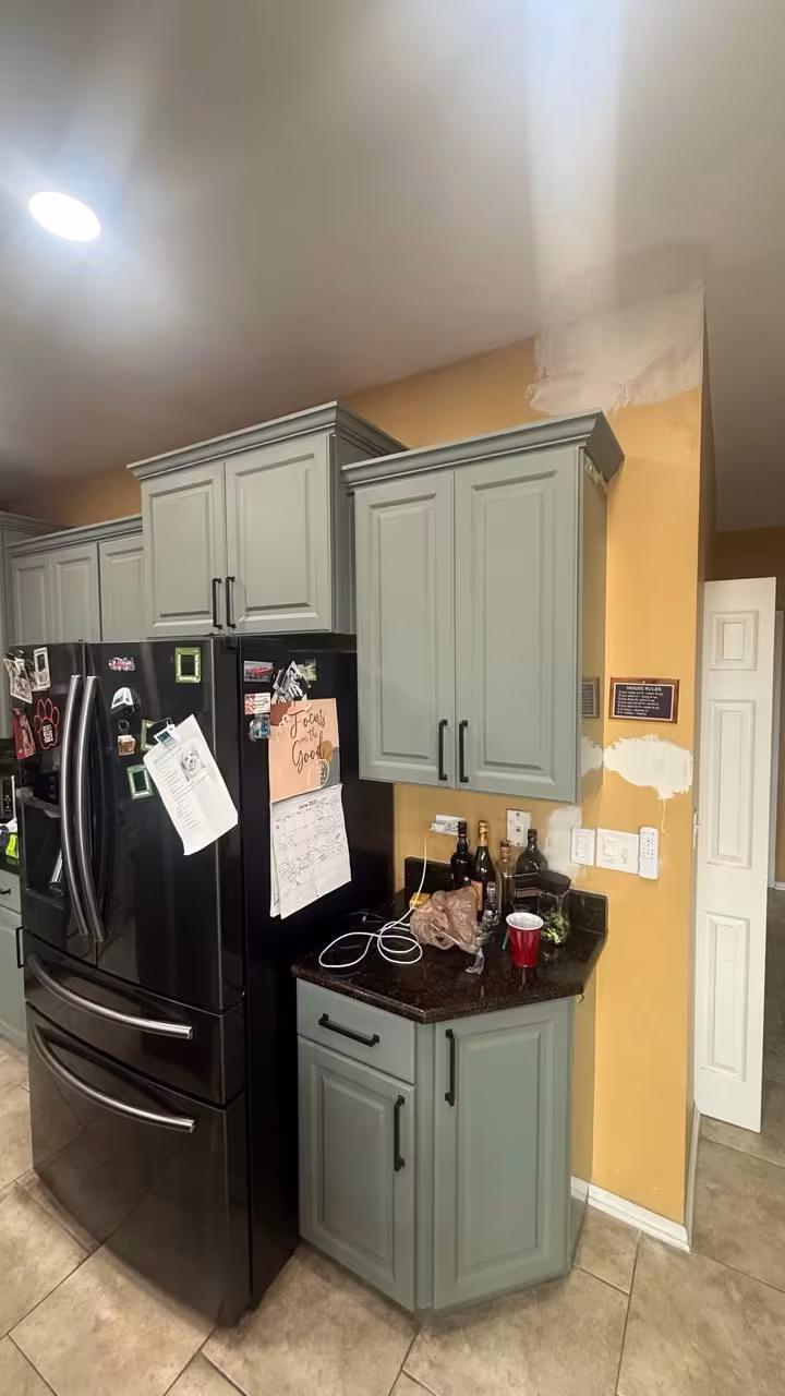 Sage gray corner cabinets and pantry beside the black refrigerator