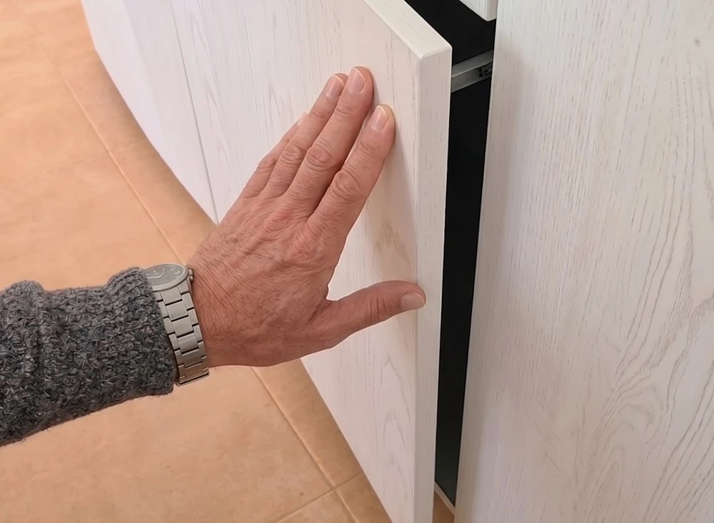 Hand pressing a handleless push-open drawer front in a compact kitchen