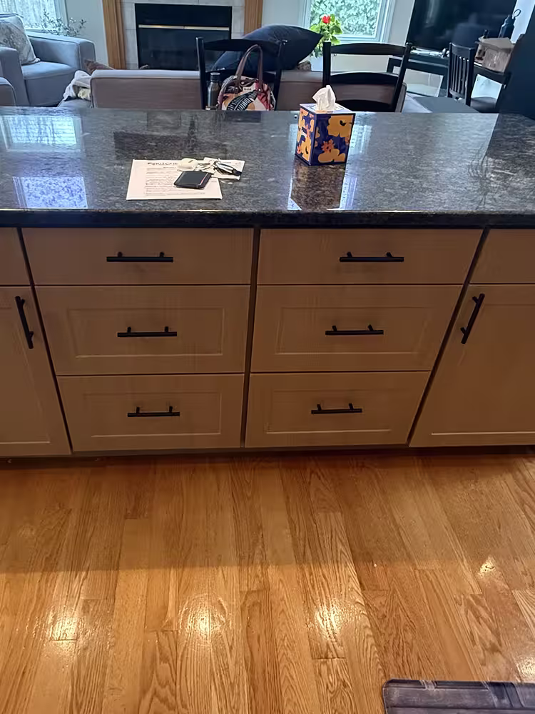 Lighter refaced drawer fronts and black bar pulls beside the granite island top
