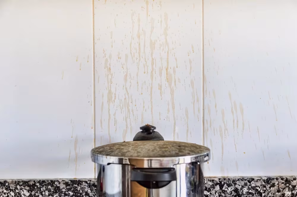 Grease streaks running down a white cabinet beside a stainless pot