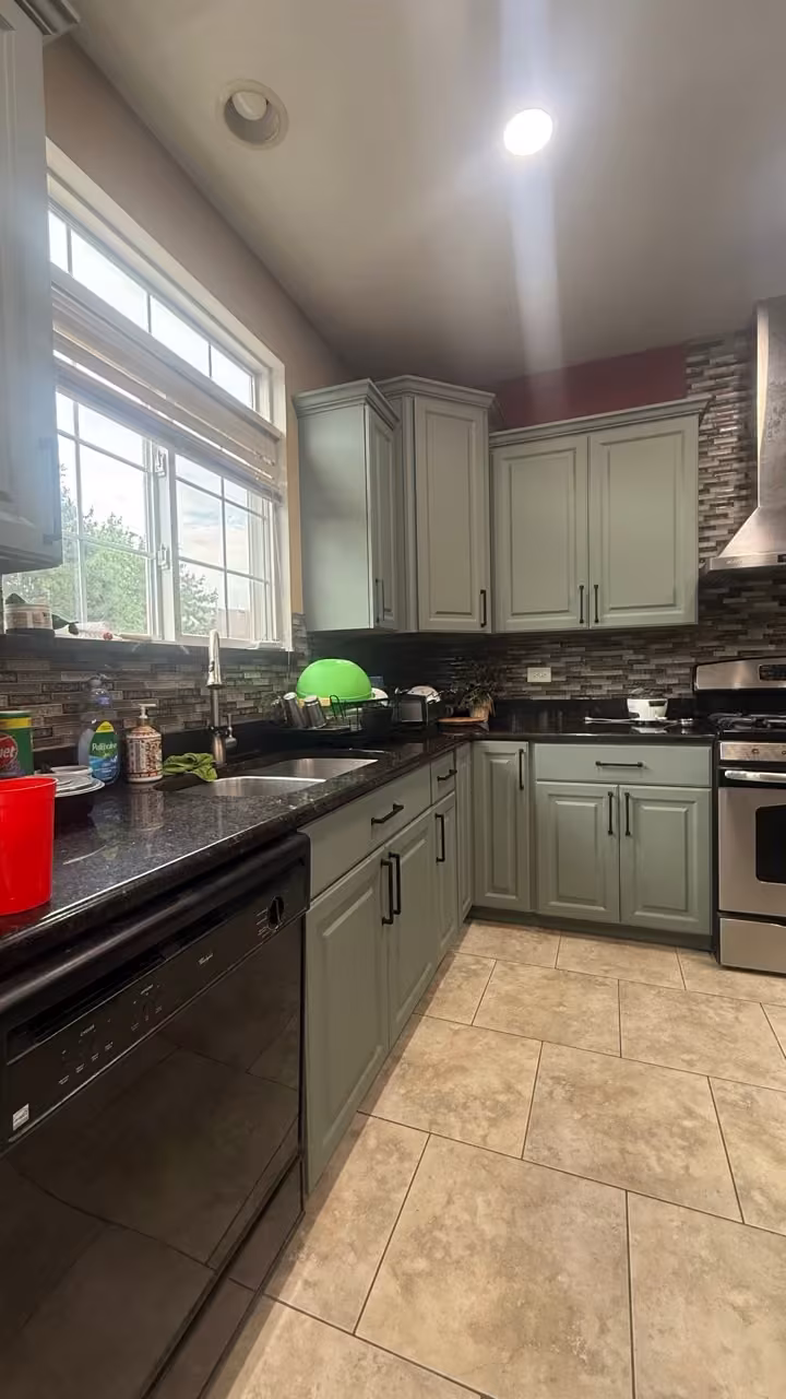 Sage gray cabinets and black counters seen from the dining side of the kitchen