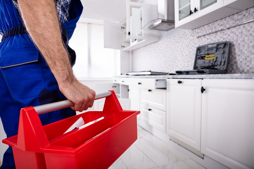 Homeowner carrying a red toolbox into a white kitchen