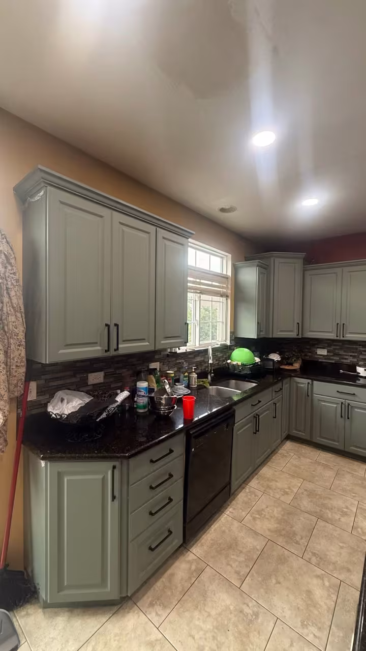 Sage gray cabinets and black countertops along the window wall after refacing