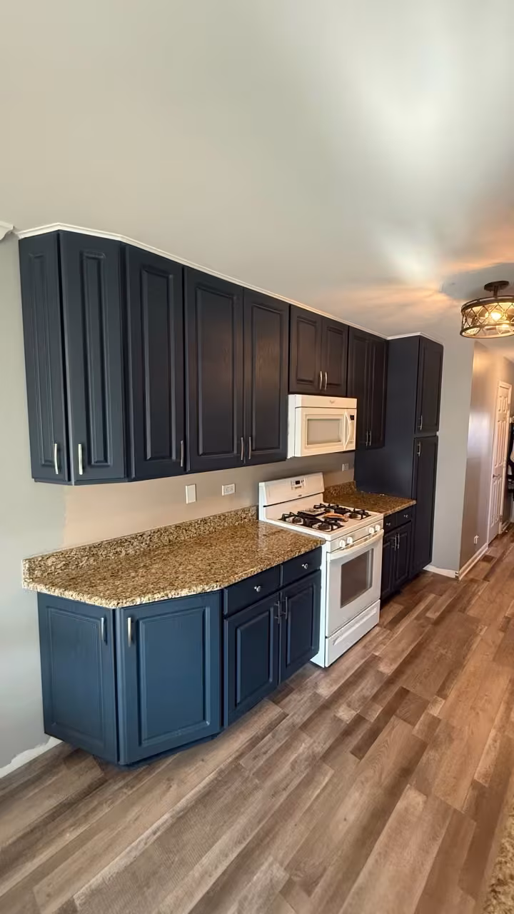 Navy blue refaced cabinets beside white appliances in the galley kitchen