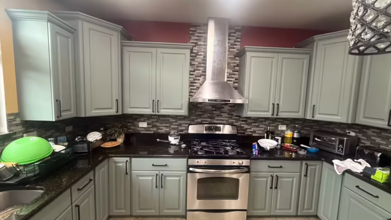 Refaced sage gray cabinets framing the stainless range hood and mosaic backsplash