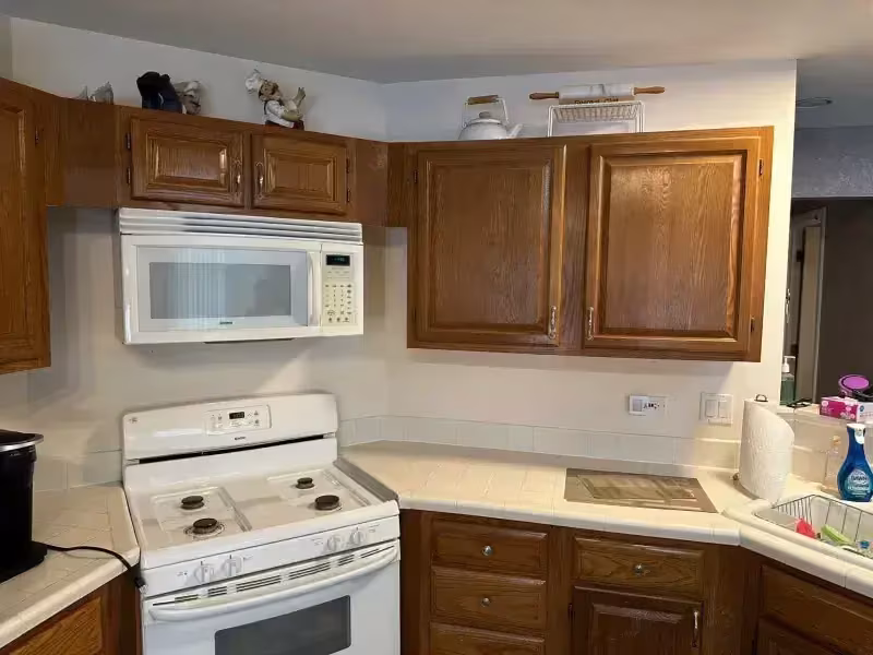 Worn oak cabinets with white appliances in a Bartlett kitchen before budget refacing