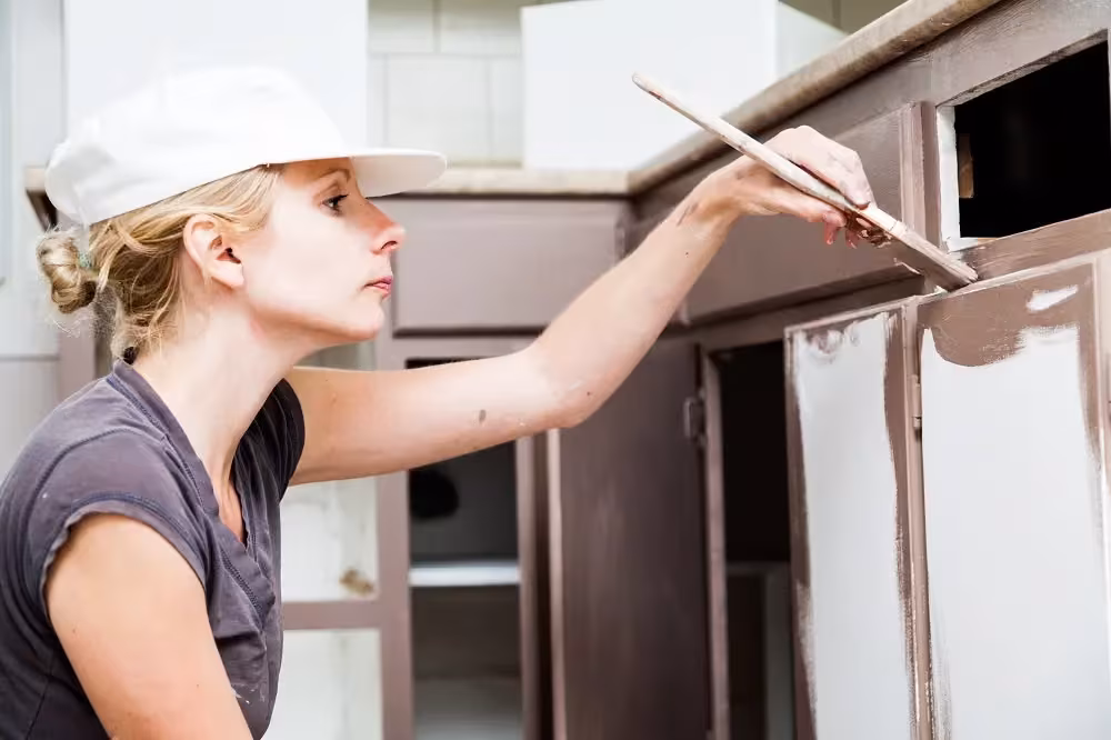 Woman in a hard hat painting a cabinet frame