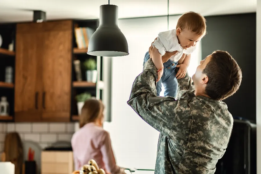 Service member in camouflage lifting a baby at home